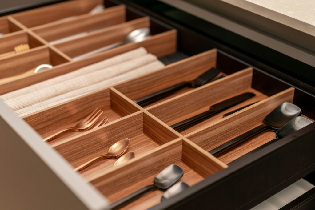 Cutlery drawer with black, gold and silver cutlery and cooking untensils with wooden details.